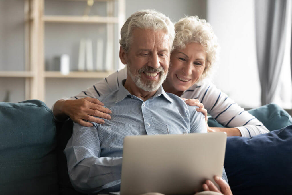 elderly couple sitting on couch while using a laptop